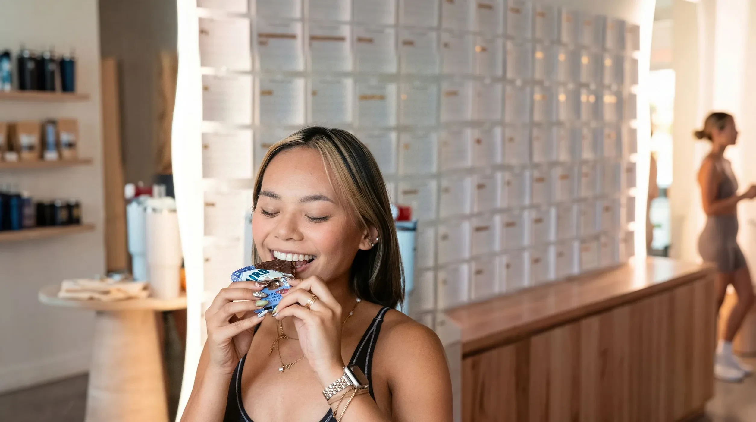 A woman smiling as she bites into a Laird Superfood bar in a bright fitness studio